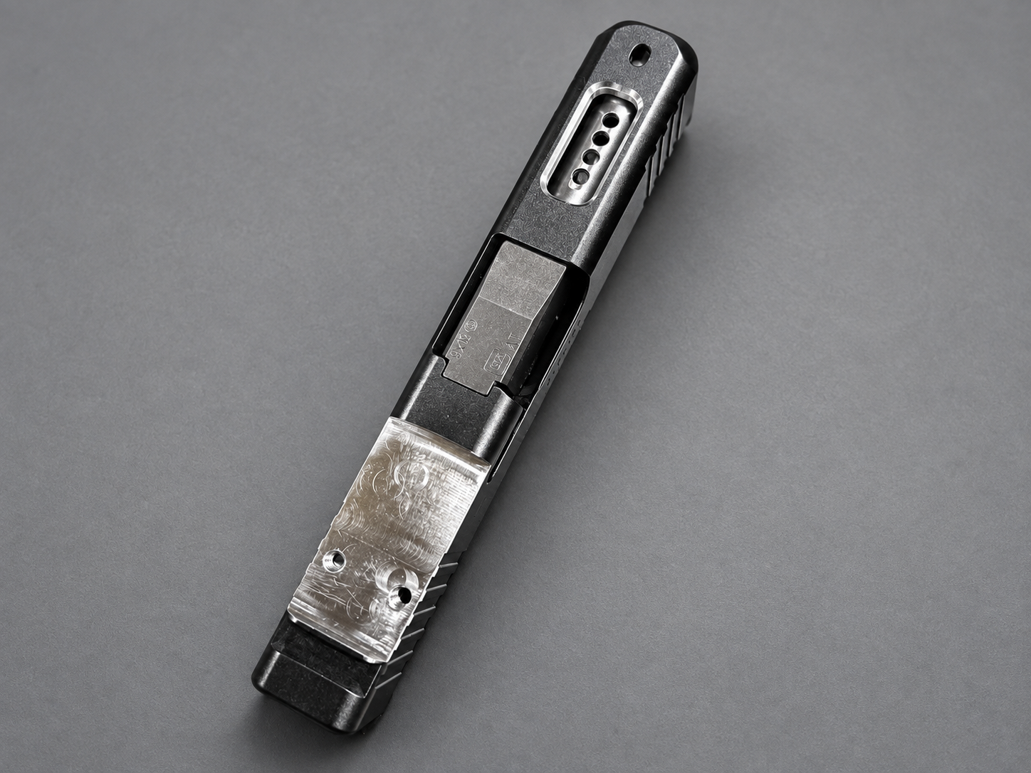 Firearm slide assembly with a machined optic mounting cut and visible barrel ports in stainless steel